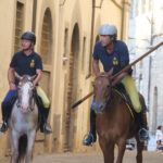 Due giostratori a cavallo percorrono l’accesso a Piazza Grande